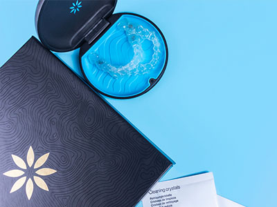 A dark blue folder with an open page displaying a toothbrush and a tube of dental floss, set against a light teal background with a patterned design.